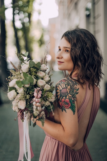 Mujer feliz y sonriente con ramo de flores en un vestido de novia rosa y anillo de bodas