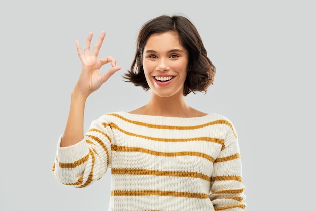 una mujer feliz y sonriente con un suéter a rayas que muestra que está bien
