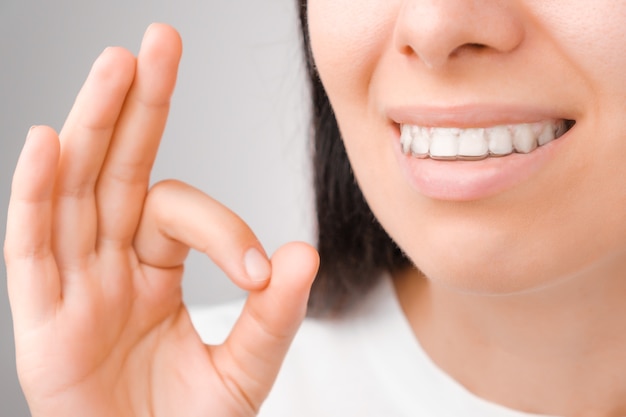 Mujer feliz con una sonrisa perfecta en alineadores transparentes en los dientes muestra signo OK