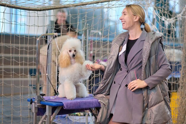 Una mujer feliz con una sonrisa en su rostro sostiene la pata de un caniche en miniatura de albaricoque