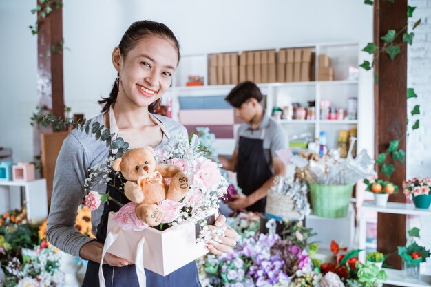 Mujer feliz sosteniendo un empaque de regalo listo para vender. Trabajando en floristería vistiendo delantal de pie con un amigo