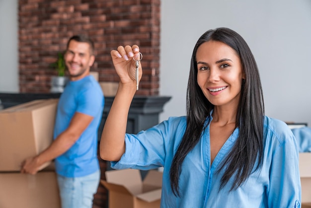 Mujer feliz sosteniendo las llaves del nuevo hogar mientras el hombre está de pie con una caja en el fondo