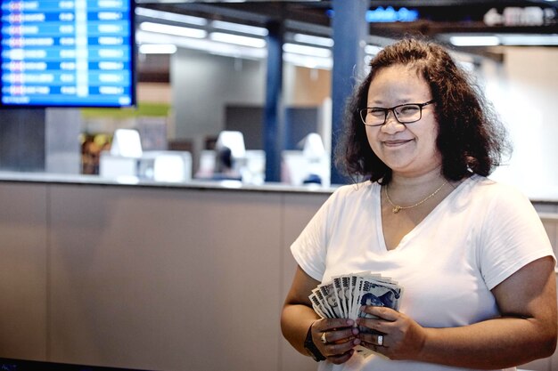 Foto mujer feliz sosteniendo moneda de papel mientras está de pie en el aeropuerto