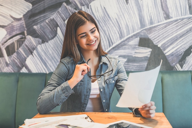 La mujer feliz sosteniendo un papel en la mesa de un café