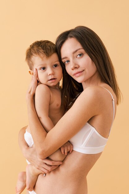 Mujer feliz sosteniendo a su bebé con fondo de color - Mujer joven usando ropa interior cuidando a su hijo pequeño - Embarazo, maternidad, personas y concepto de expectativa