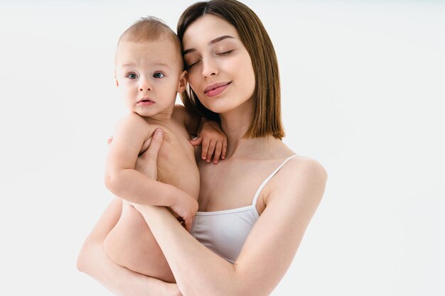 Mujer feliz sosteniendo a su bebé con fondo de color - Mujer joven usando ropa interior cuidando a su hijo pequeño - Embarazo, maternidad, personas y concepto de expectativa