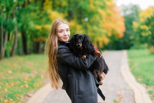 Mujer feliz sosteniendo su perrito en brazos, parque de otoño