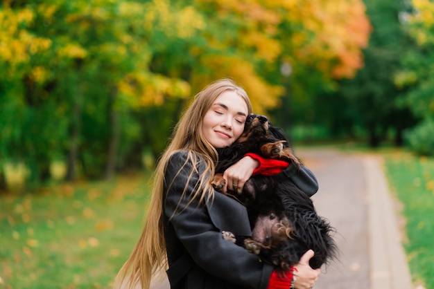 Mujer feliz sosteniendo su perrito en brazos, parque de otoño