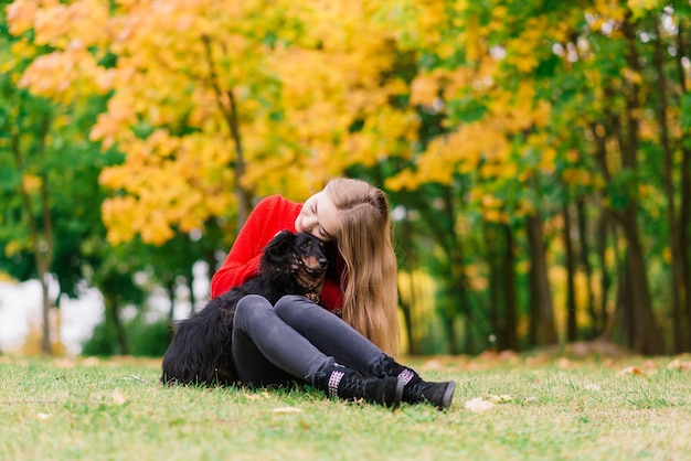 Mujer feliz sosteniendo su perrito en brazos, parque de otoño
