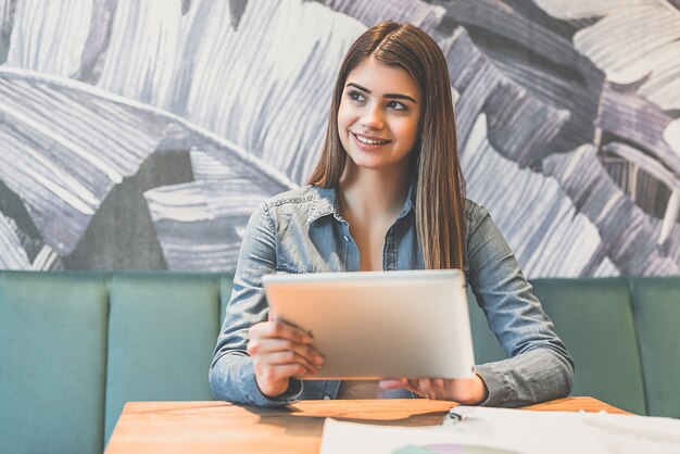 La mujer feliz sosteniendo una tableta en la mesa