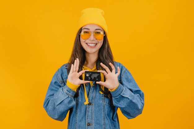 Mujer feliz sosteniendo tarjeta de crédito aislada sobre fondo amarillo
