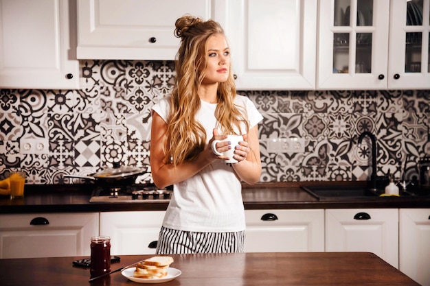 Mujer feliz sosteniendo una taza de café mientras está de pie en su cocina