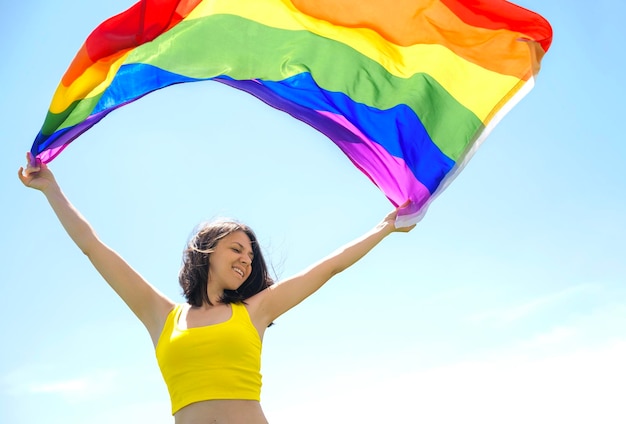 Una mujer feliz sostiene una bandera del arco iris ondeando en el viento