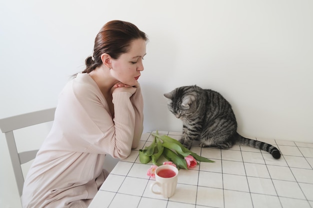 mujer feliz y su gato oliendo tulipanes rosados frescos por la mañana en casa