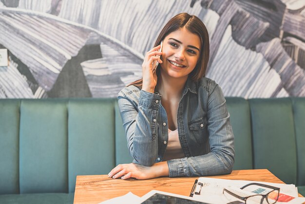 La mujer feliz telefonea en la mesa de un café