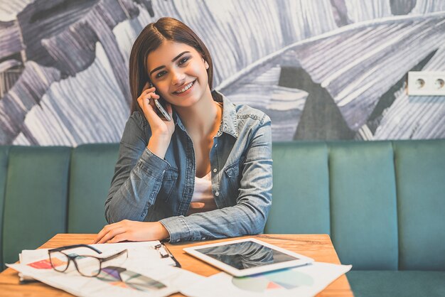 La mujer feliz telefonea en la mesa de un café