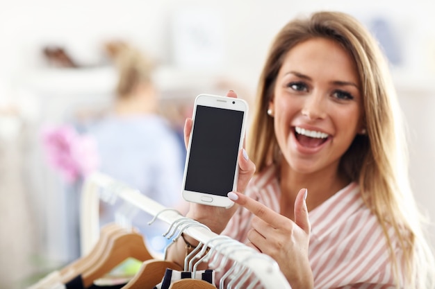 Foto mujer feliz, en, tienda de ropa, tenencia, smartphone