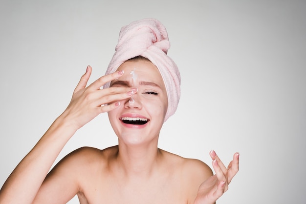 Mujer feliz con una toalla en la cabeza después de la ducha pone crema en la cara