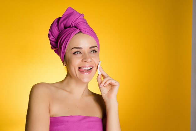 Mujer feliz con una toalla en la cabeza quita el maquillaje con un disco de algodón