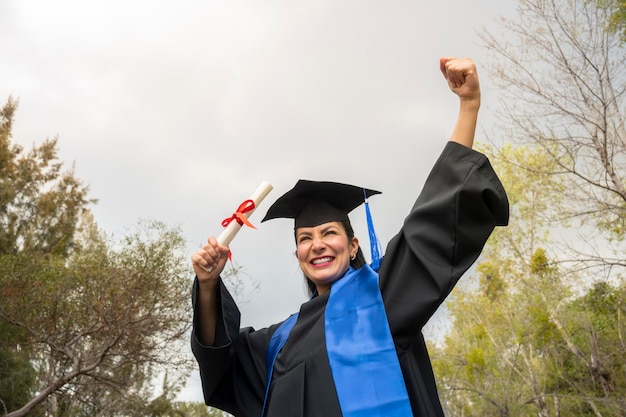 Mujer feliz con toga y birrete escolar celebrando su graduación al aire libre