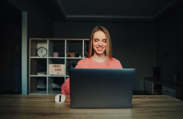 Foto mujer feliz trabajando en casa en una mesa de internet en una laptop con una sonrisa en la cara mirando la pantalla