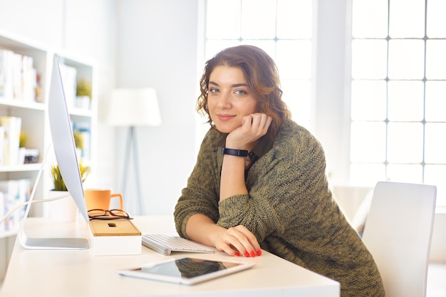 Mujer feliz trabajando usando múltiples dispositivos en un escritorio en casa