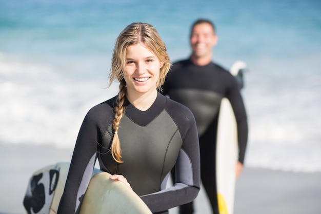 Mujer feliz en traje de neopreno con una tabla de surf en la playa