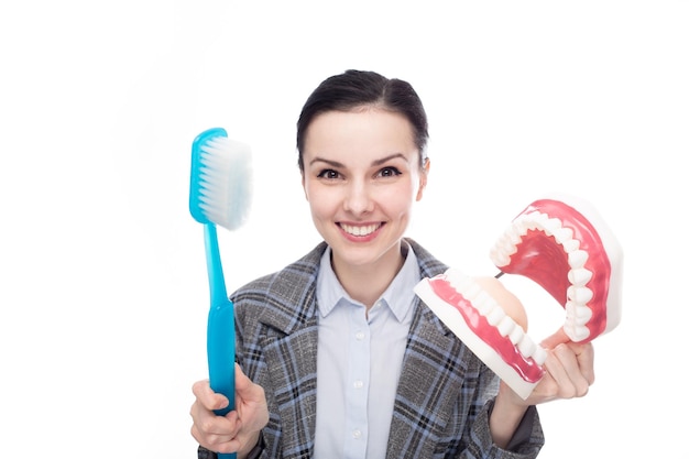 Mujer feliz en traje de oficina sosteniendo un gran cepillo de dientes y una gran maqueta de mandíbula con dientes de fondo blanco