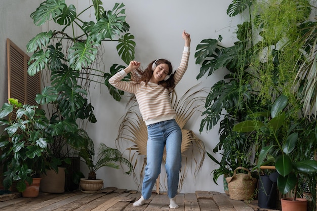 Una mujer feliz usa audífonos inalámbricos escuchando música bailando en el jardín de su casa con plantas tropicales