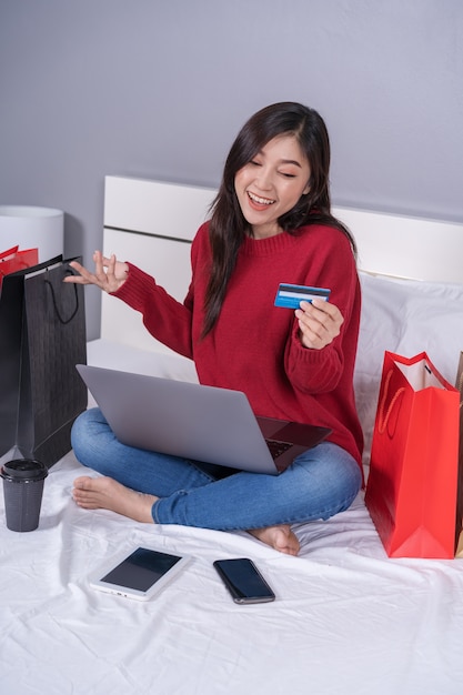 Mujer feliz usando una computadora portátil para compras en línea con tarjeta de crédito en la cama