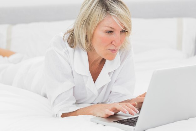 Mujer feliz usando su computadora portátil en su cama