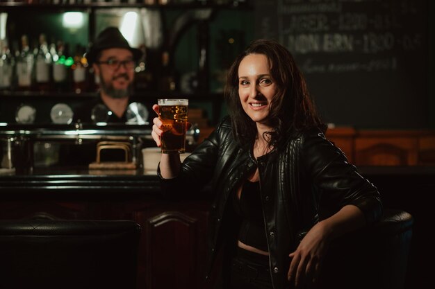 Mujer feliz con un vaso de cerveza ligera en la barra del bar