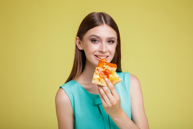 Mujer feliz con vestido azul aguamarina con fondo amarillo. Deliciosa rebanada de pizza Modelo come