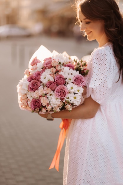 Una mujer feliz con un vestido blanco al atardecer con un ramo de flores en la ciudad