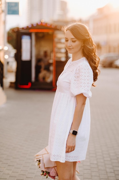 Una mujer feliz con un vestido blanco al atardecer con un ramo de flores en la ciudad