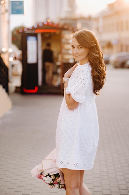 Una mujer feliz con un vestido blanco al atardecer con un ramo de flores en la ciudad