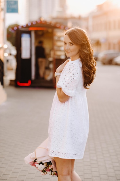 Una mujer feliz con un vestido blanco al atardecer con un ramo de flores en la ciudad