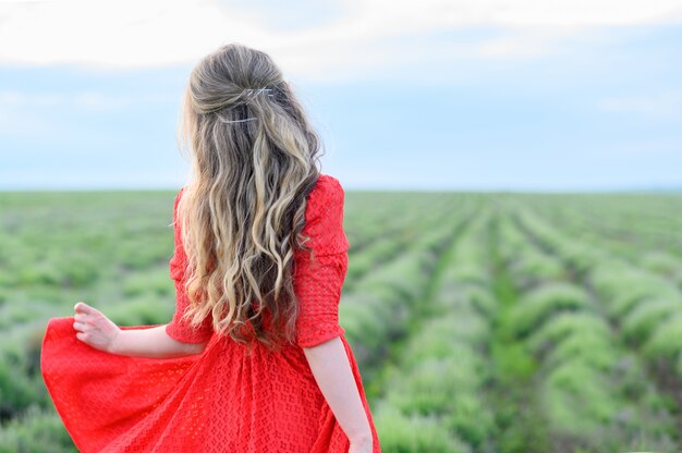 Mujer feliz en vestido rojo bailando y saltando en el campo de lavanda