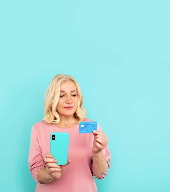 Mujer feliz en el vestido rosa con tarjeta de crédito con móvil.