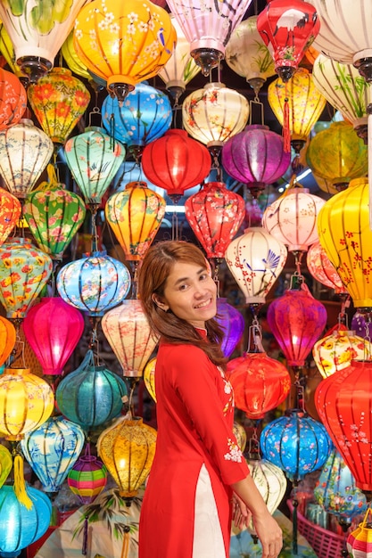 Mujer feliz con un vestido vietnamita de Ao Dai con farolillos coloridos que hacen turismo en la antigua ciudad de Hoi An en el centro de Vietnam, punto de referencia para las atracciones turísticas Concepto de viaje de Vietnam y el sudeste