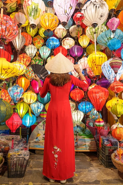 Mujer feliz con un vestido vietnamita de Ao Dai con farolillos coloridos que hacen turismo en la antigua ciudad de Hoi An en el centro de Vietnam, punto de referencia para las atracciones turísticas Concepto de viaje de Vietnam y el sudeste