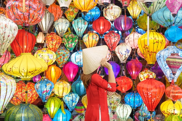 Mujer feliz con un vestido vietnamita de Ao Dai con farolillos coloridos que hacen turismo en la antigua ciudad de Hoi An en el centro de Vietnam, punto de referencia para las atracciones turísticas Concepto de viaje de Vietnam y el sudeste