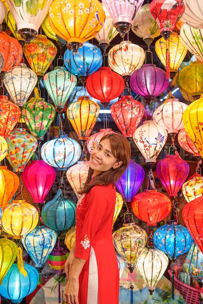 Foto mujer feliz con un vestido vietnamita de ao dai con farolillos coloridos que hacen turismo en la antigua ciudad de hoi an en el centro de vietnam, punto de referencia para las atracciones turísticas concepto de viaje de vietnam y el sudeste