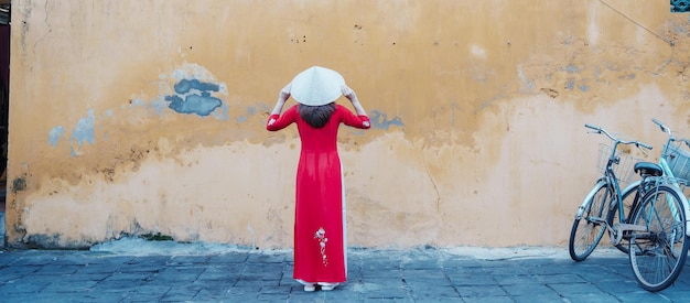 Mujer feliz con vestido vietnamita Ao Dai y sombrero viajero haciendo turismo en la antigua ciudad de Hoi An en el centro de Vietnam, punto de referencia y popular por las atracciones turísticas Vietnam y el concepto de viaje del sudeste