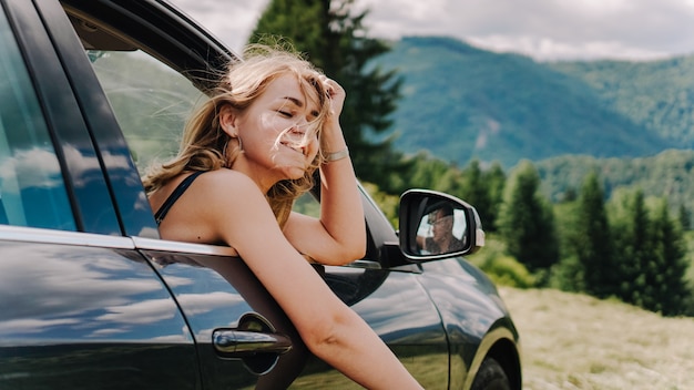 Mujer feliz viaja en coche por las montañas. Concepto de vacaciones de verano. Mujer por la ventana disfrutando de vistas a la montaña