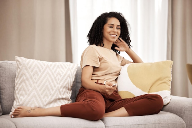 Mujer feliz y viendo televisión en un sofá, relájese y riéndose de películas y películas de comedia en su casa Mujer negra de televisión y transmisión de entretenimiento y humor en un sofá en una sala de estar