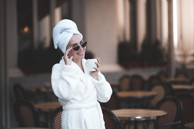 Mujer feliz vistiendo una cómoda bata de baño blanca y sosteniendo una taza de café recién hecho