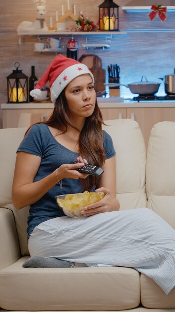 Mujer festiva viendo la televisión y comiendo patatas fritas del tazón de fuente