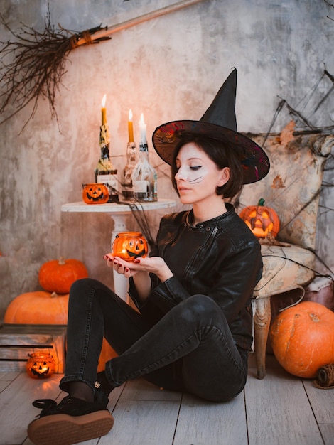 Mujer en una fiesta de disfraces de Halloween a imagen de una bruja maquillada en el fondo de velas encendidas y calabaza