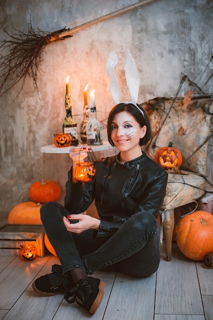 Mujer en una fiesta de disfraces de Halloween a imagen de orejas de liebre y maquillaje en el fondo de velas y calabazas encendidas